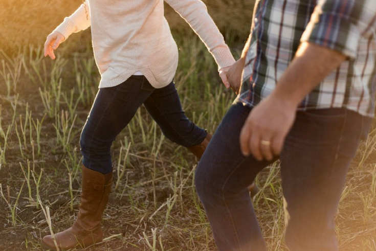 Husband and wife walk, hand in hand, through a field.